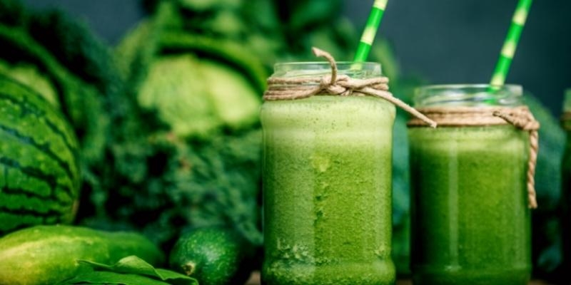 Blended green smoothie with ingredients on wooden table