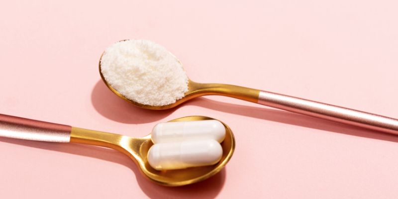 Spoons of capsules and powder on pink background