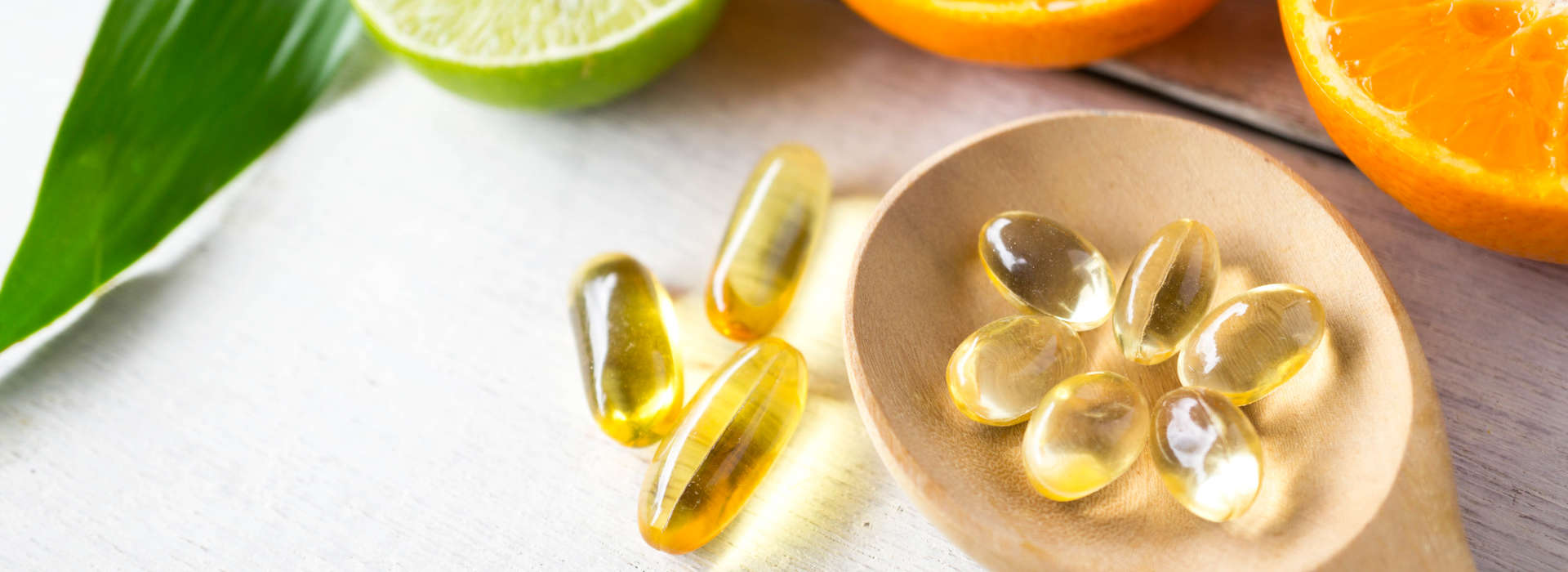 softgels on a wooden spoon next to oranges and lime